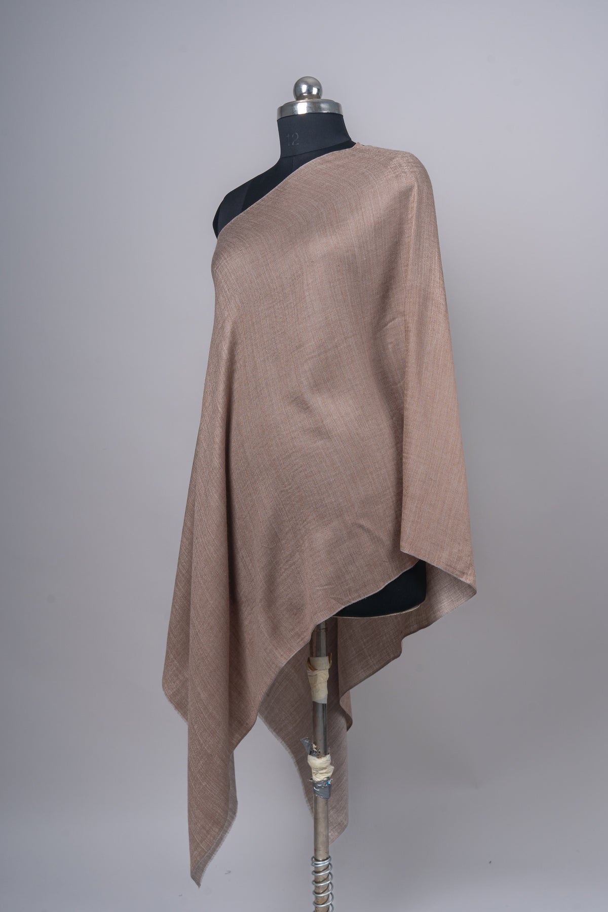 Angled view of the almond-beige stole draped on a mannequin, with the grey underside visible beneath the lower fold.