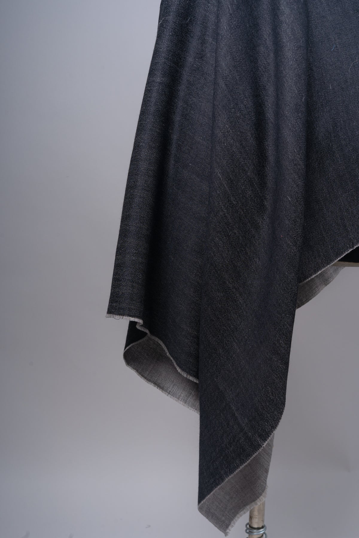 Detail of the charcoal stole’s hanging folds, with the slate-grey reverse visible along the turned edge