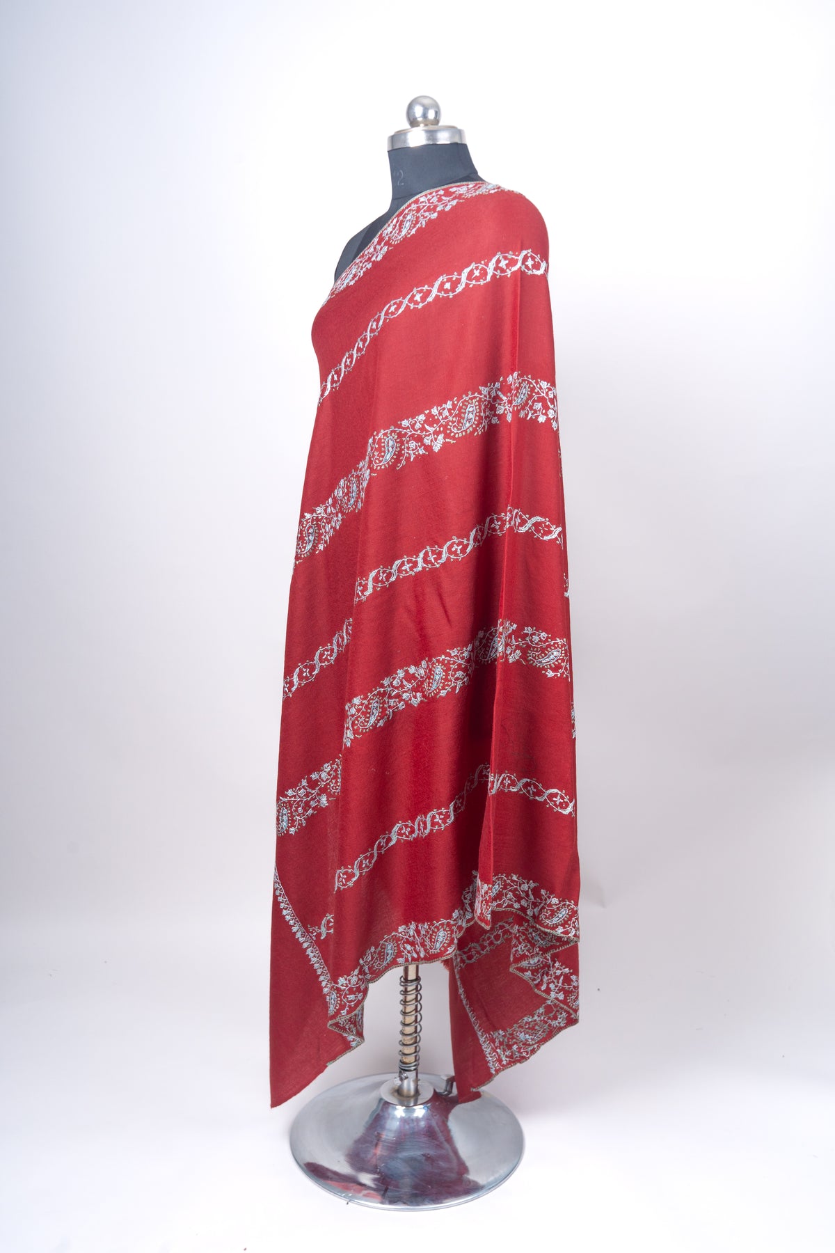 Full side view of the crimson shawl draped over a mannequin, with pale blue embroidered bands and patterned edges