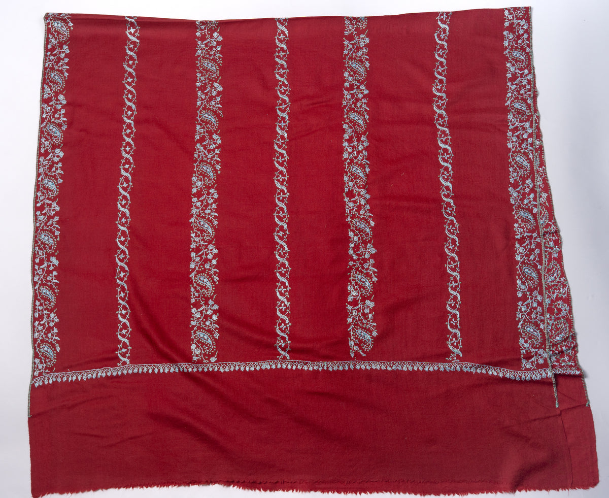 Crimson shawl laid flat, showing parallel pale blue floral and scrolling bands above a plain end panel
