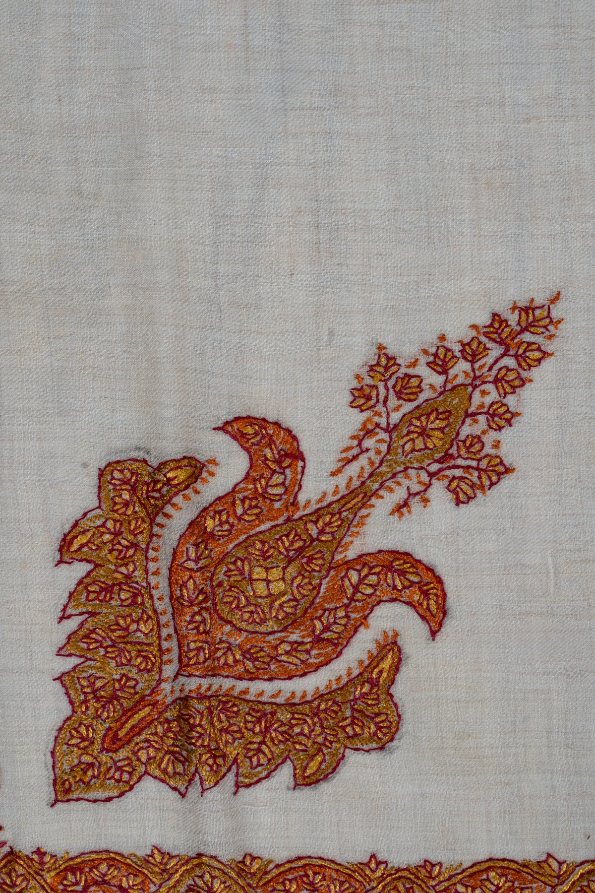 Close-up of a saffron and maroon floral motif with curling lobes and a leafy stem on ivory rumal fabric