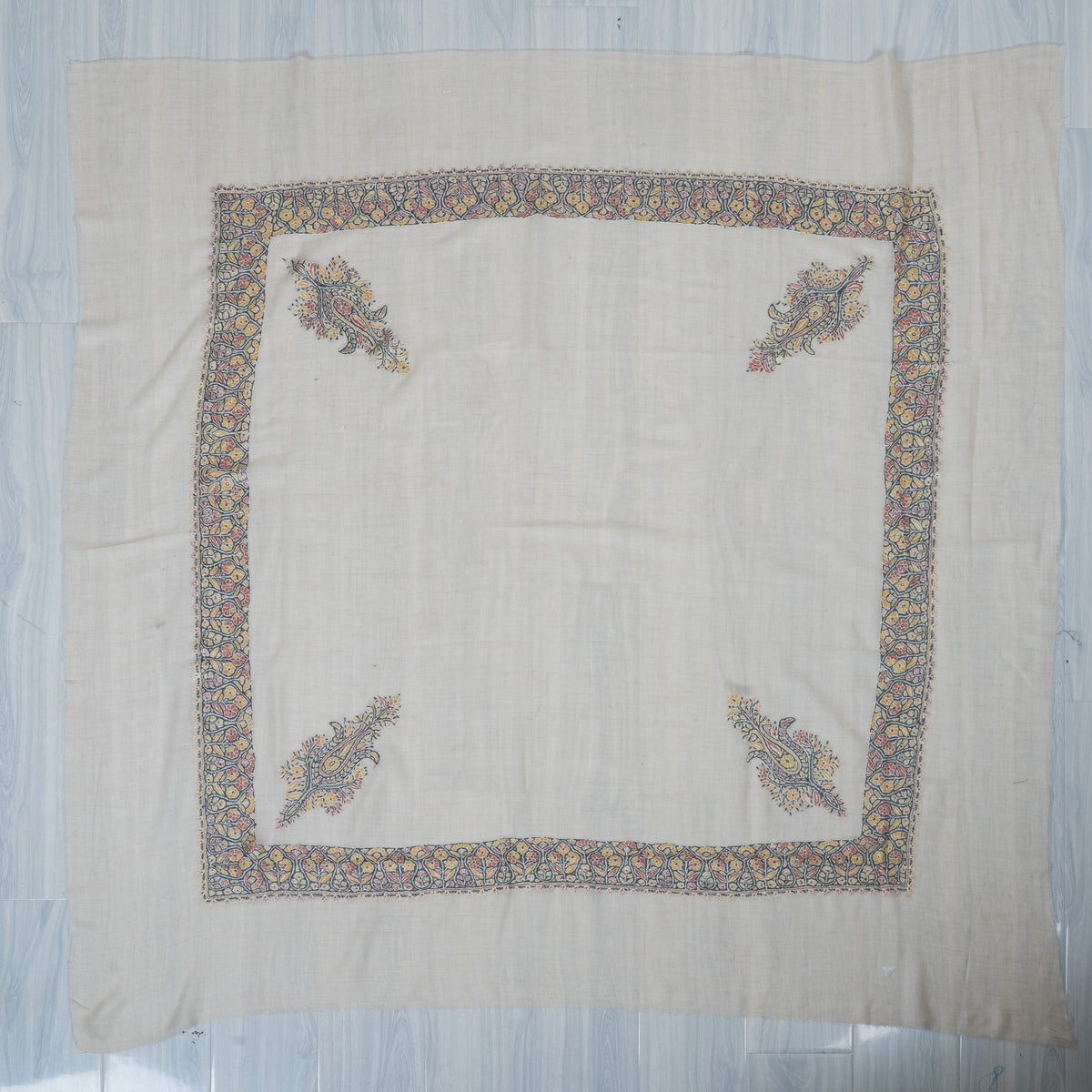 Ivory cashmere rumal laid flat, with a square pastel floral border and four paisley corner motifs