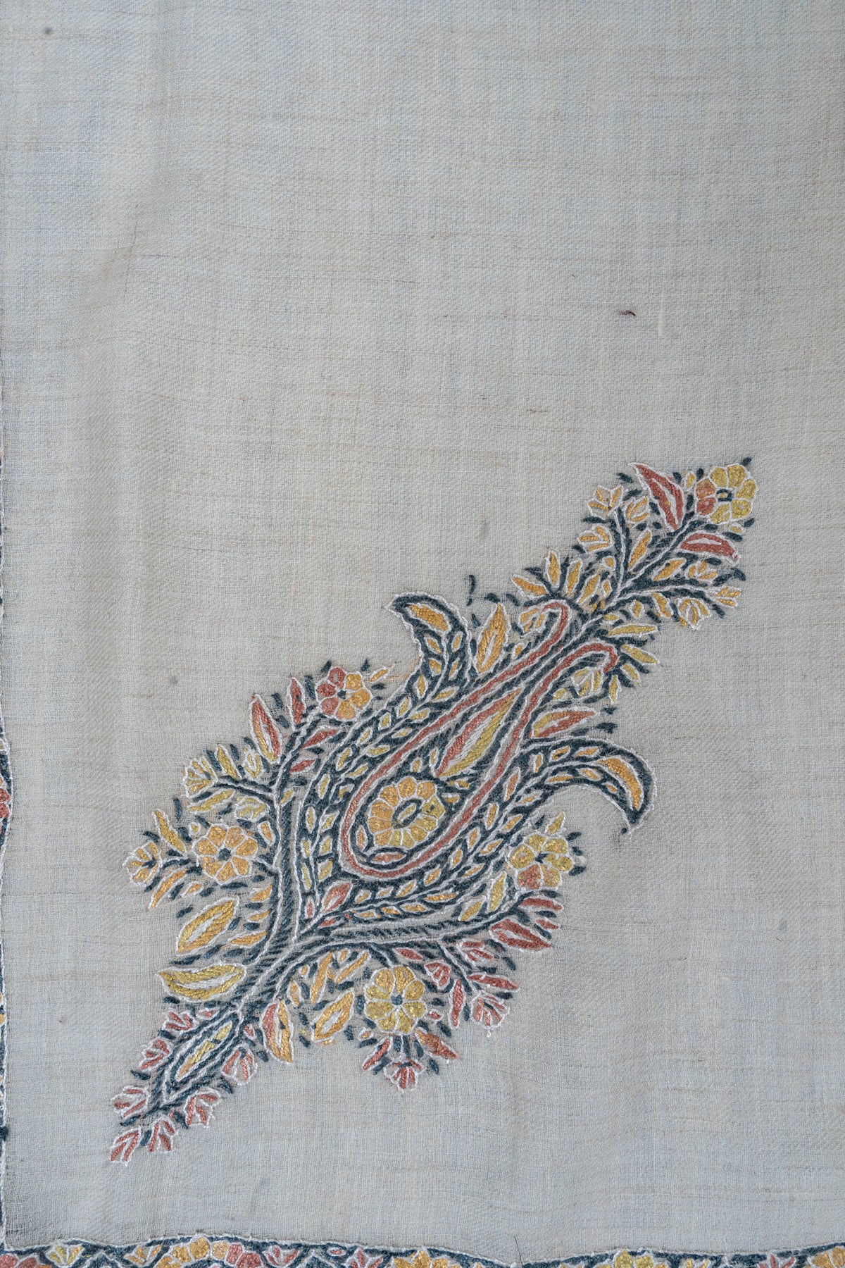 Close-up of a coral, yellow and blue floral paisley embroidered on ivory cashmere