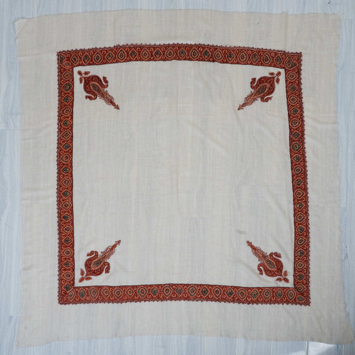 Square ivory rumal laid flat with four rust-red and green corner paisleys, a detailed medallion border and a plain centre