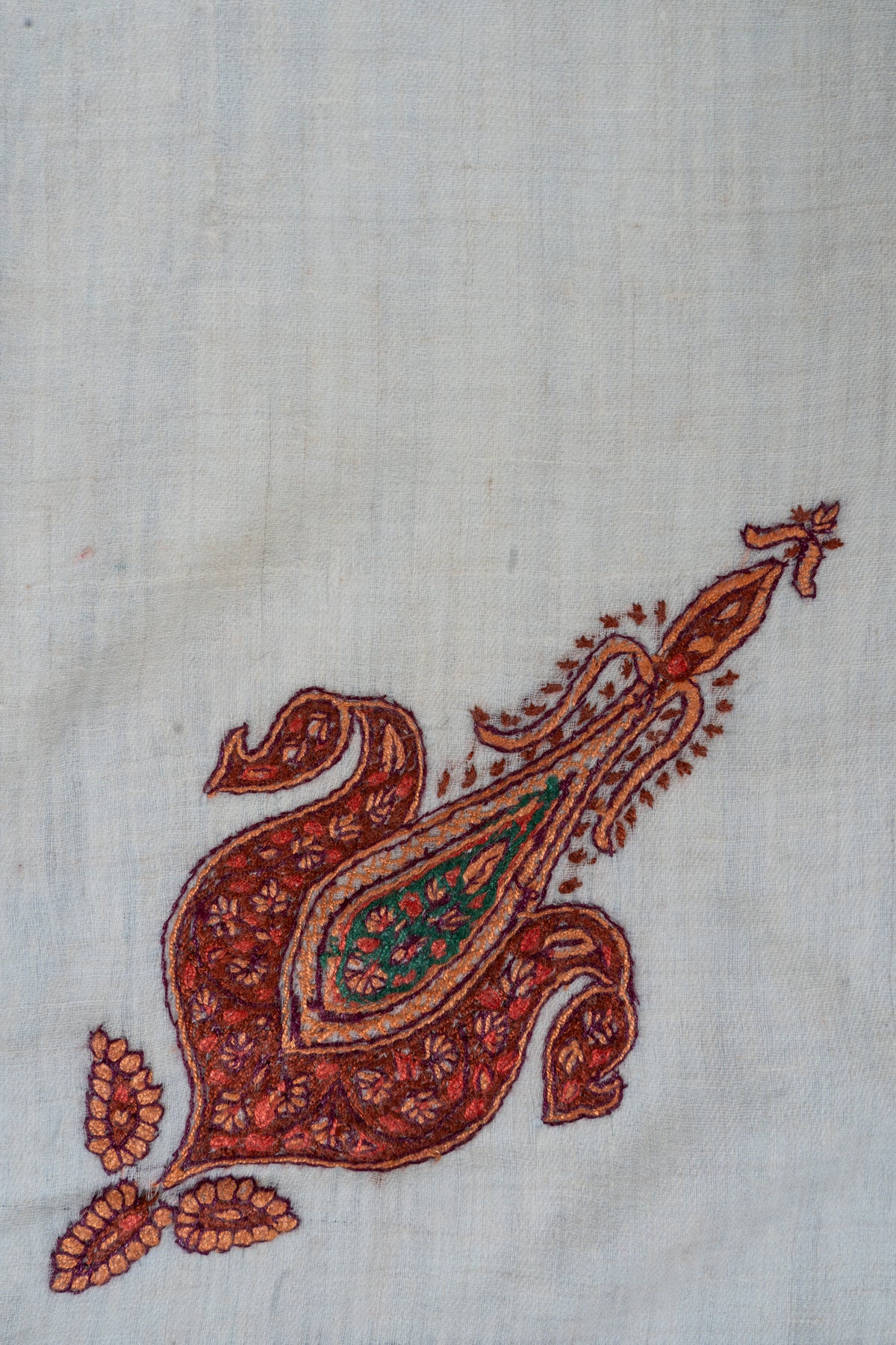 Close-up of a rust-red and copper paisley with green floral filling embroidered on ivory rumal fabric
