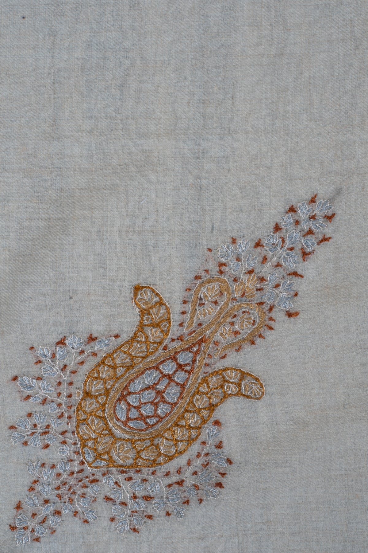 Close-up of a honey-gold Sozni floral motif with a pale blue teardrop centre and delicate leafy sprays on cream fabric