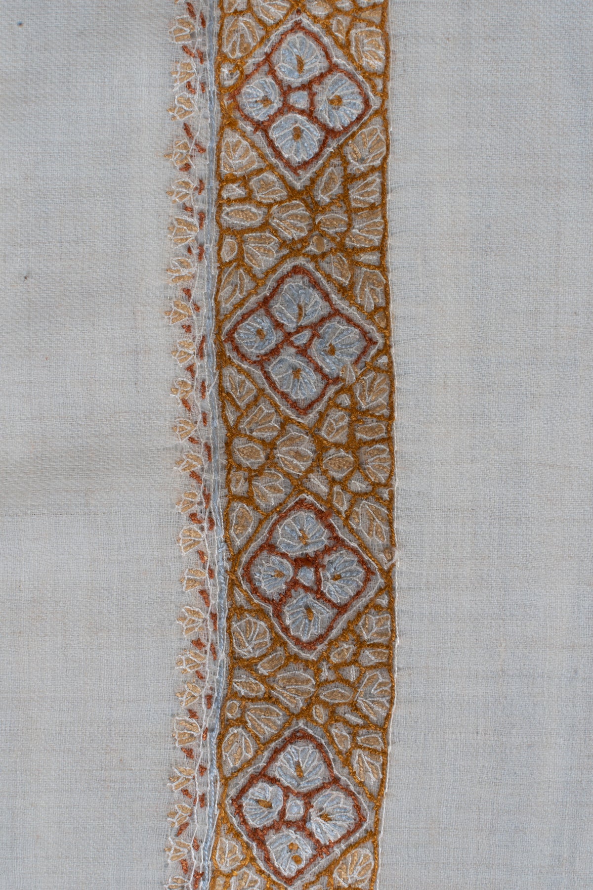 Close-up of a honey-gold rumal border with pale blue four-petal motifs inside diamonds and fine leafy stitching