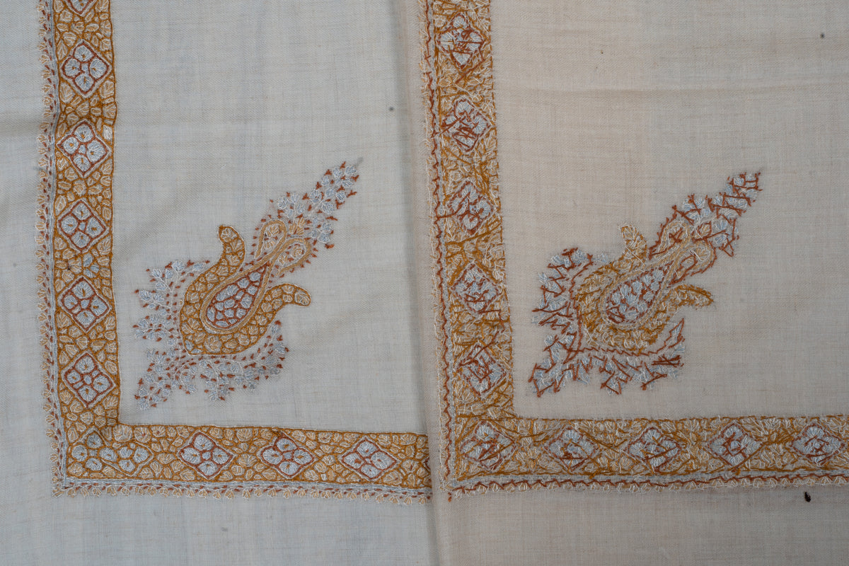 Overlapping cream rumal corners showing both sides of honey-gold and pale blue Sozni floral motifs and geometric borders