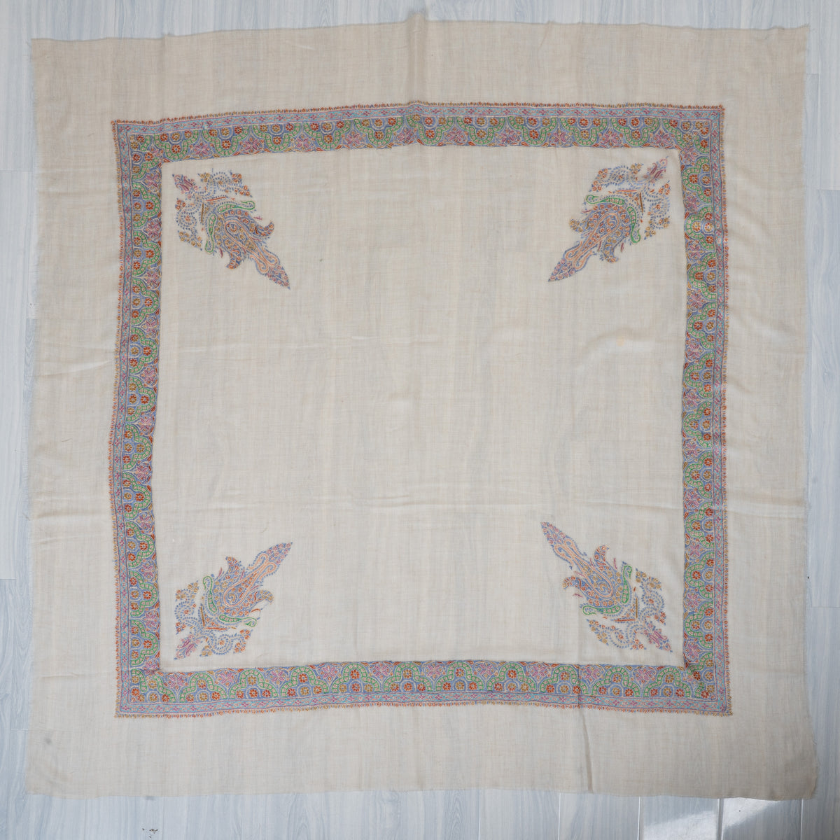 Cream square cashmere rumal laid flat with multicoloured Sozni floral borders, four corner paisleys and a plain centre.