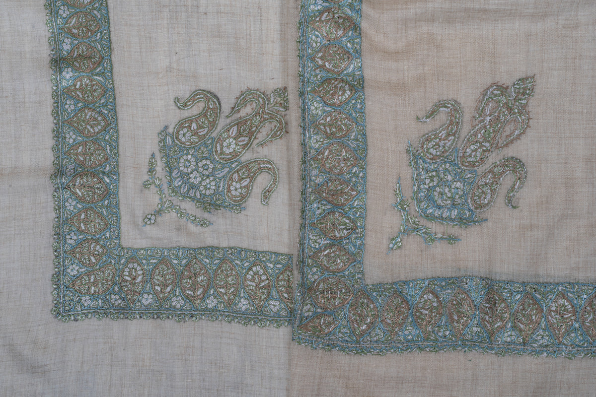 Overlapping beige rumal corners showing the front and reverse of sage and aqua embroidery