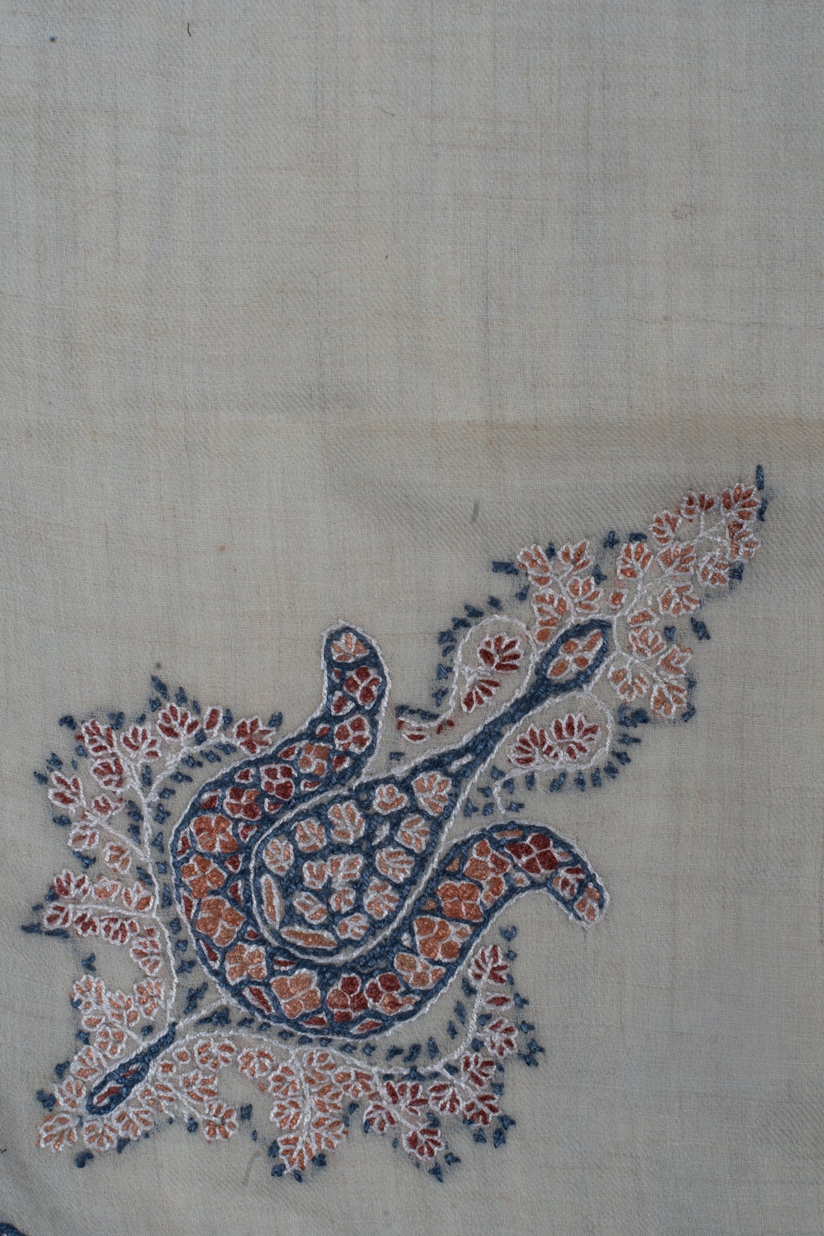 Close-up of an indigo, coral and rust Sozni floral motif with a teardrop centre and delicate leafy sprays on ivory fabric