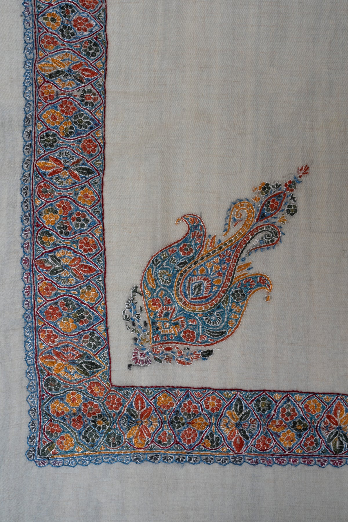 Cream rumal corner with a blue, saffron and red Sozni border and a matching paisley motif