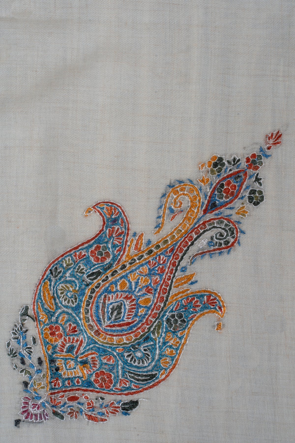 Close-up of a blue, saffron and red paisley embroidered with small flowers on cream cashmere