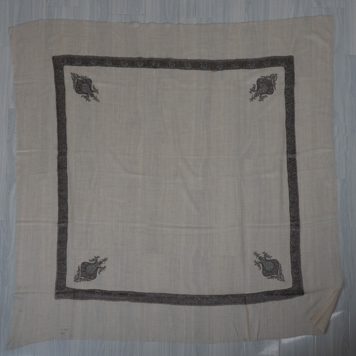 Cream cashmere rumal laid flat, with a square grey-blue border and four matching corner motifs