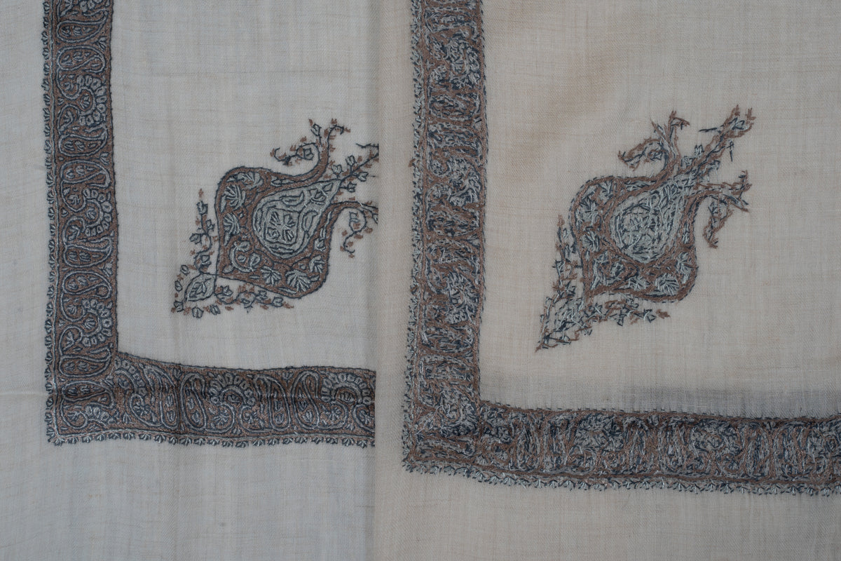 Overlapping cream rumal corners showing the front and reverse of grey-blue embroidery