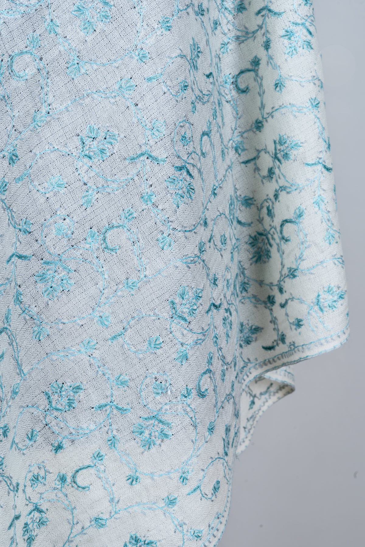 Hanging stole detail with fine pale blue flowers and curving stems across white fabric beside the narrow border.