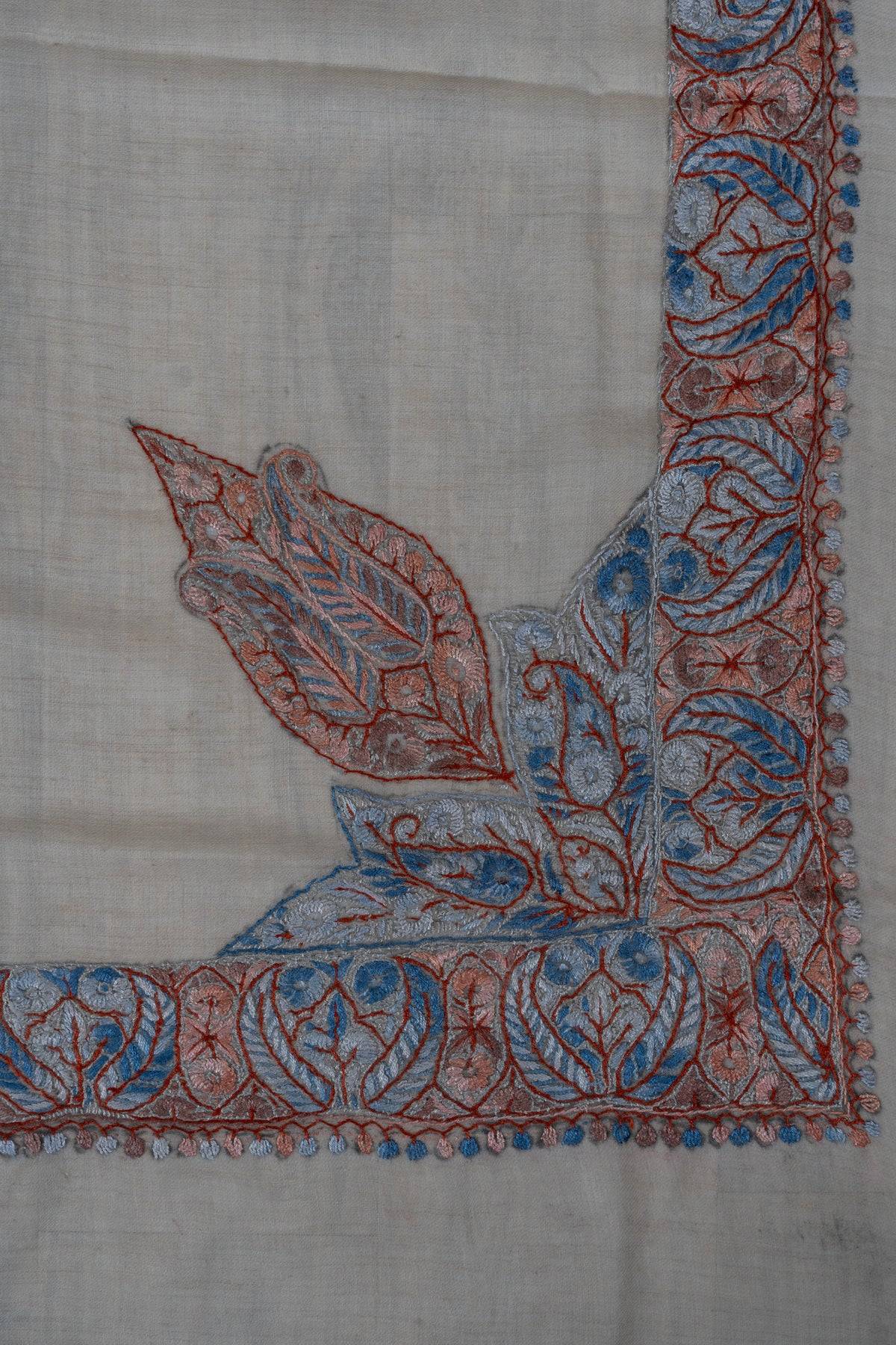 Beige rumal corner with a large coral and powder-blue Sozni leaf arrangement connected to the patterned border