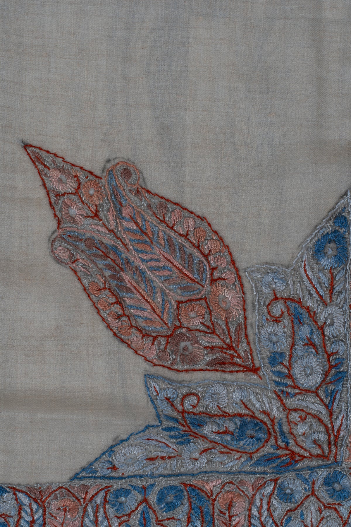 Close-up of a pointed coral and powder-blue Sozni leaf panel with fine floral filling on beige rumal fabric