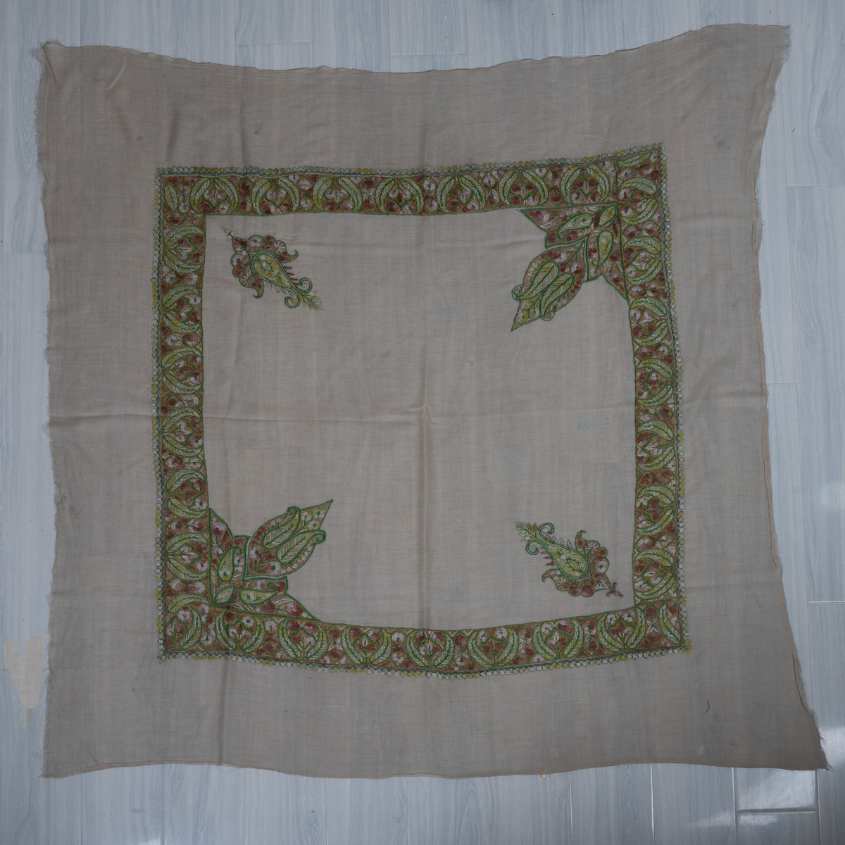 Pale beige square cashmere rumal laid flat, with a green and rose leafy border and four ornate corner motifs