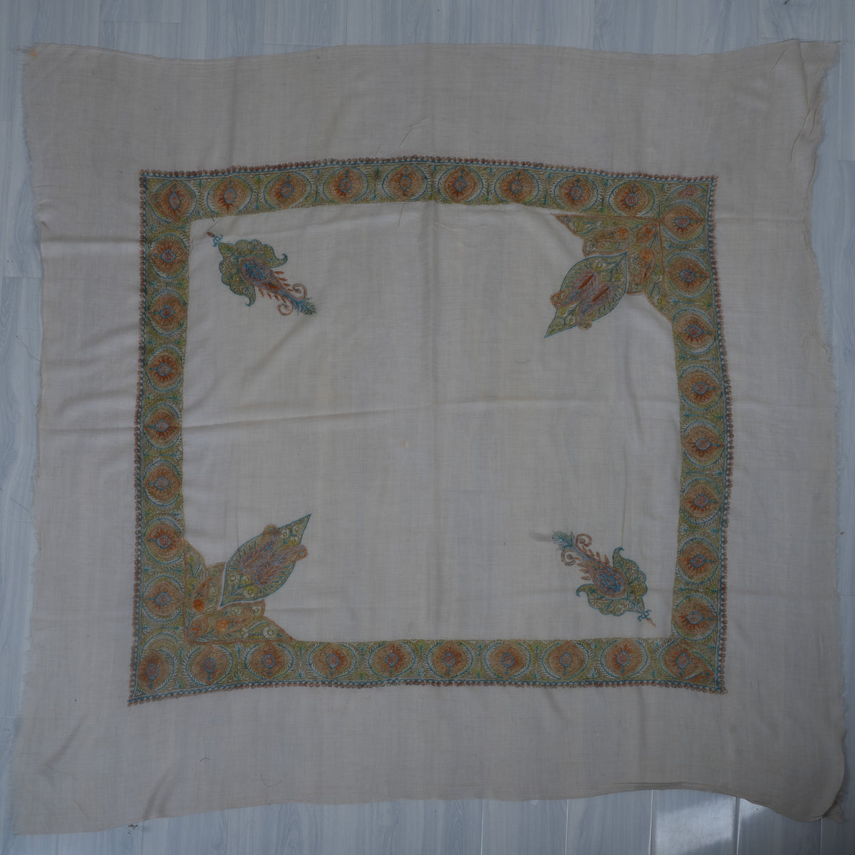 Pale square cashmere rumal laid flat with amber and blue Sozni medallion borders, two paisleys and two large leafy corners.