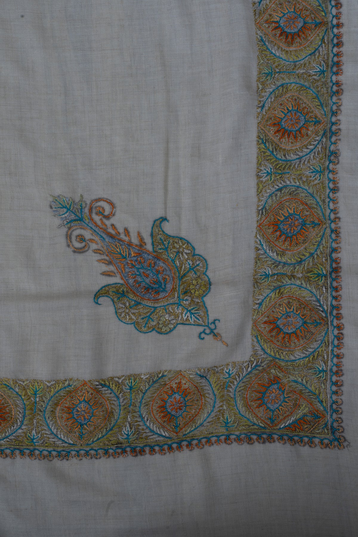 Corner of a pale cashmere rumal with an amber and blue Sozni paisley and circular floral medallion borders.