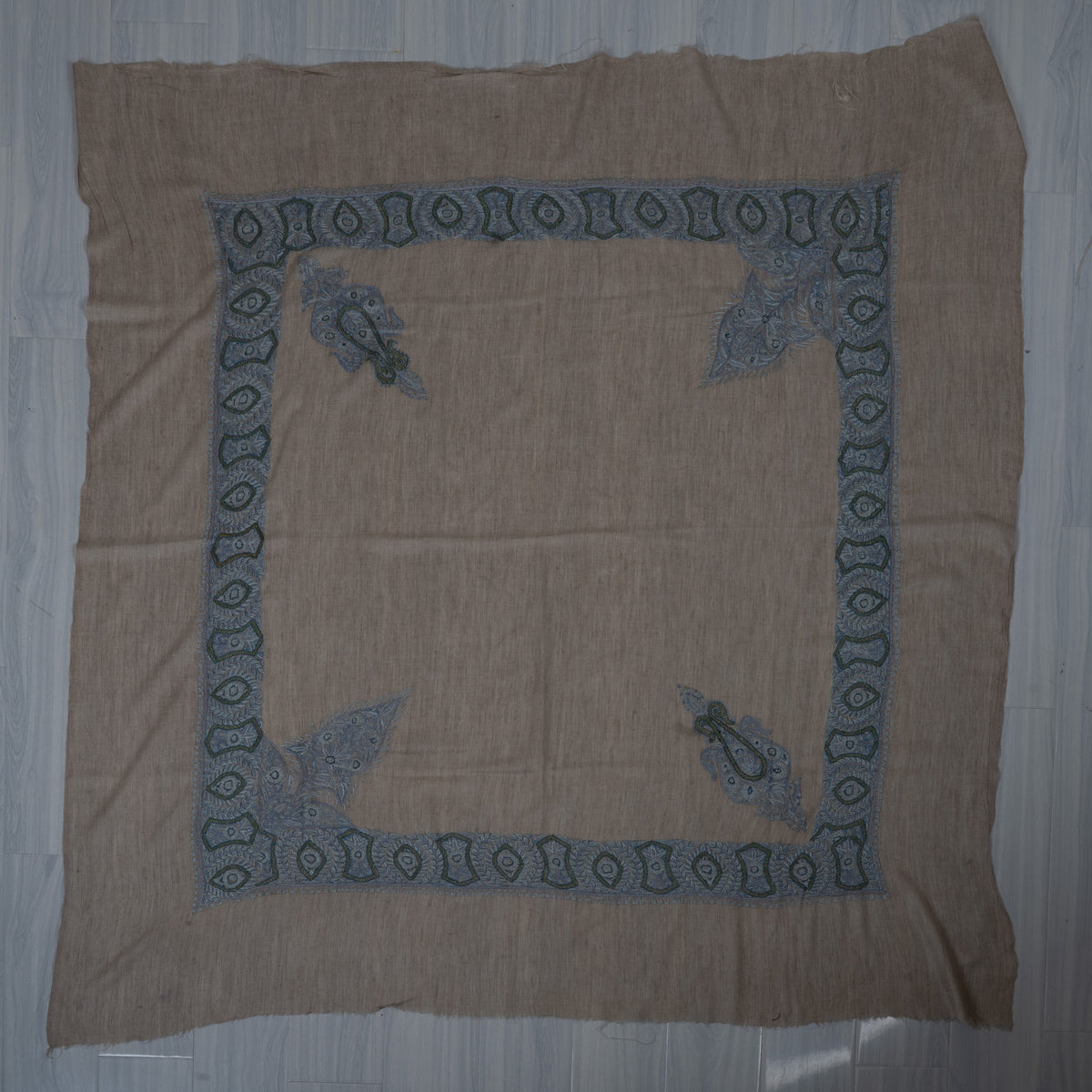 Taupe-beige cashmere rumal laid flat, with blue geometric borders, two large and two smaller corner designs