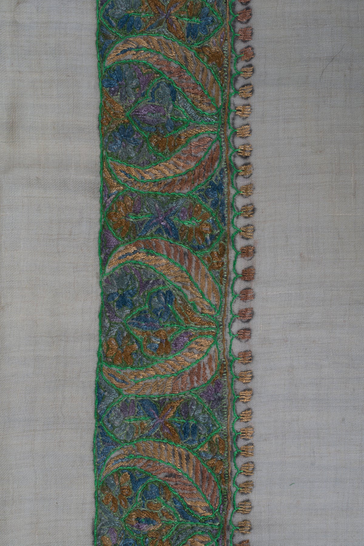 Close-up of flowing green-outlined leaves and fine blue and gold embroidery along the rumal's border