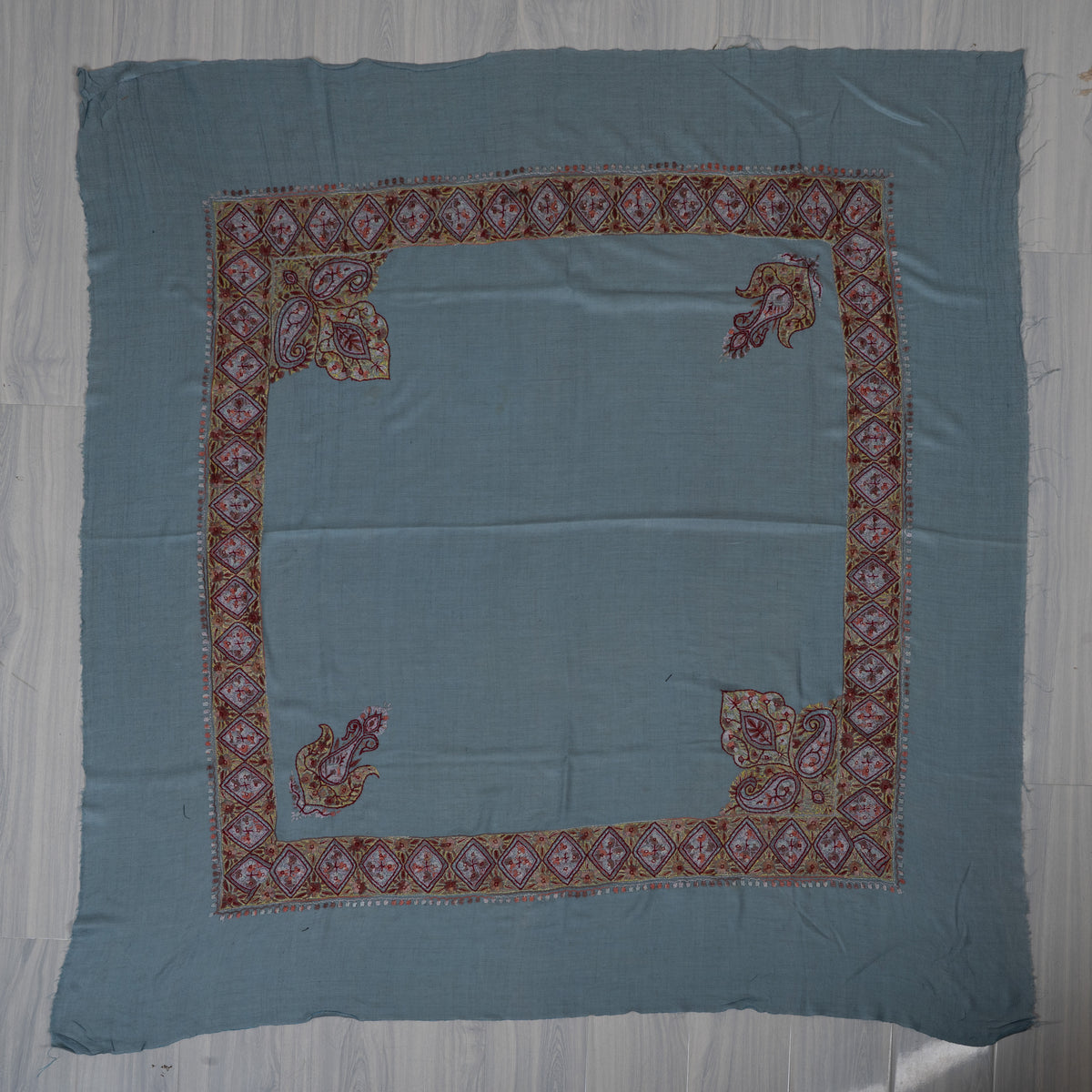 Sky-blue square cashmere rumal laid flat with garnet and gold Sozni diamond borders, two paisleys and two large leafy corners.