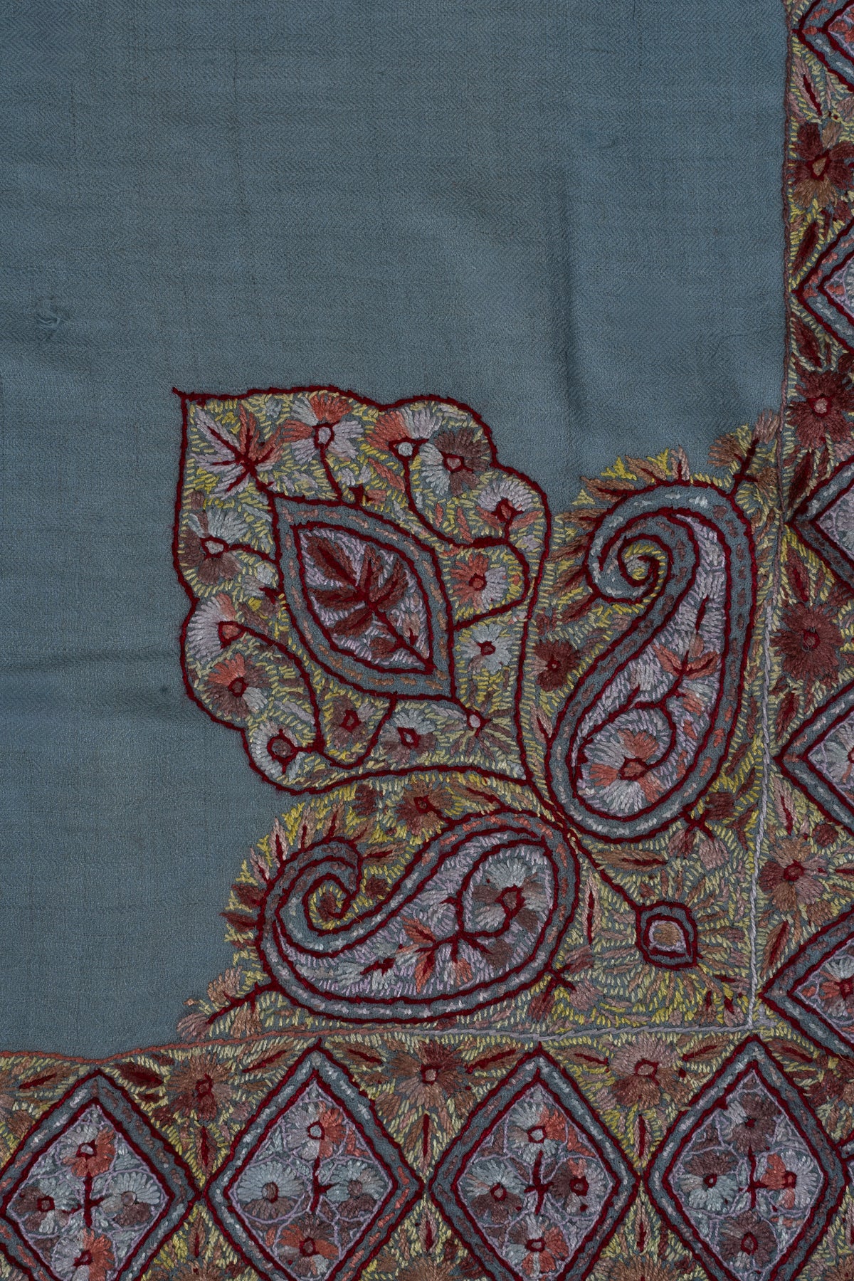 Close-up of a Sozni corner motif with pale paisleys, gold leaves and garnet outlines on sky-blue cashmere.