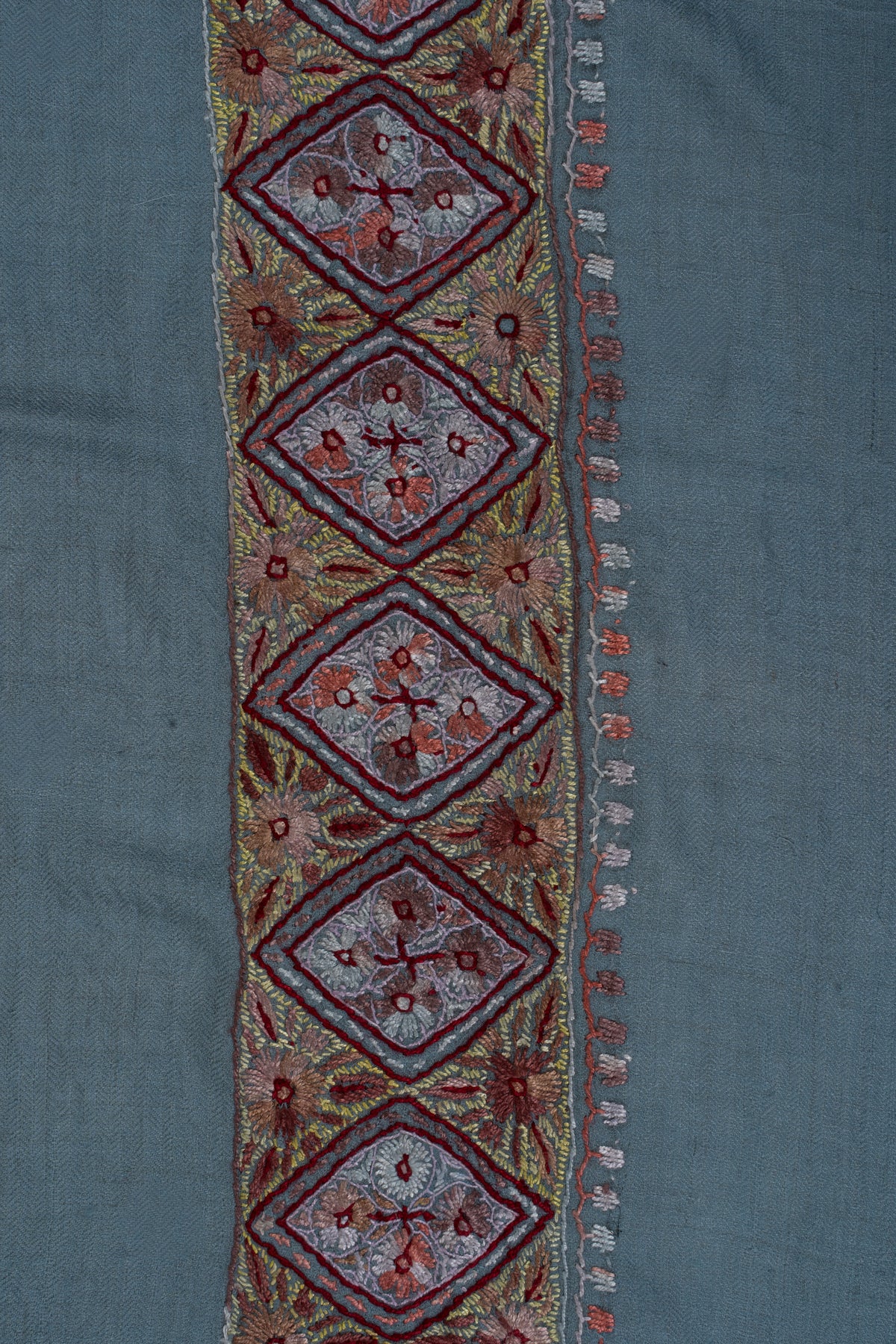 Close-up of a Sozni border with garnet-outlined diamond panels, pale floral centres and gold leaves on sky-blue cashmere.