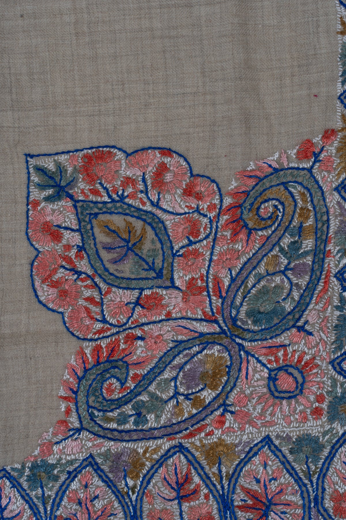 Close-up of blue-outlined Sozni paisleys and a coral floral leaf panel with sage and golden filling on beige fabric