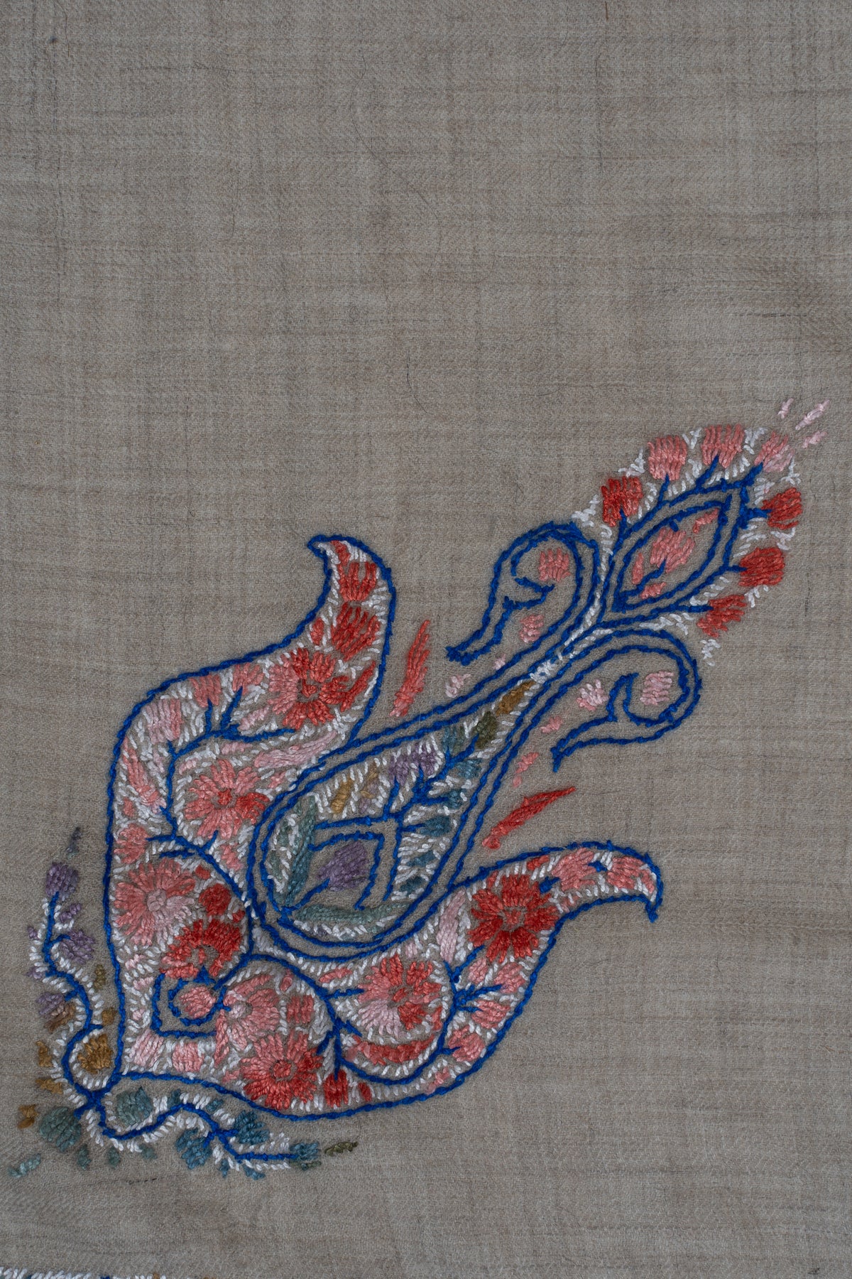 Close-up of a small coral Sozni paisley with deep blue outlines and curling tips on beige rumal fabric