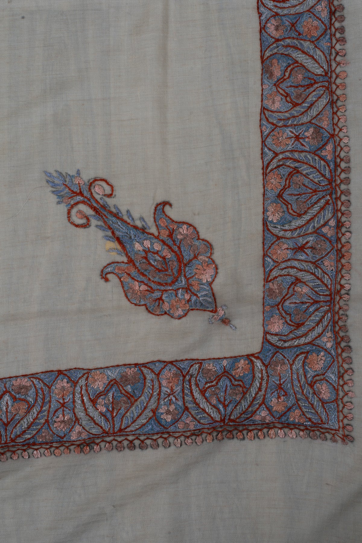 Corner of a beige cashmere rumal with a blue and dusky-rose Sozni paisley inside matching leafy borders.