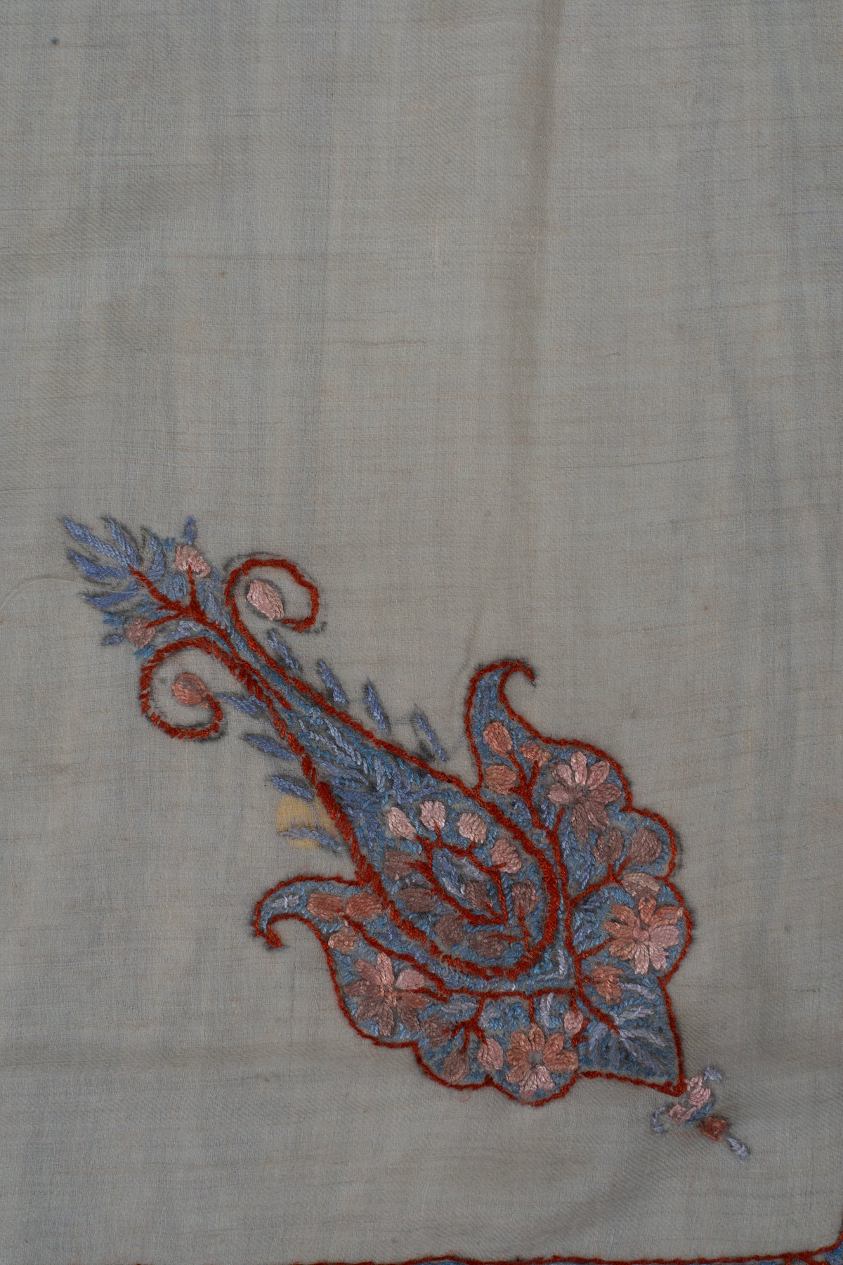 Close-up of a blue and dusky-rose Sozni paisley with a curled tip and fine floral details on beige cashmere.
