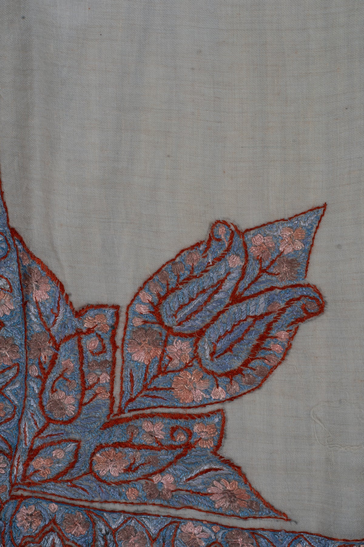 Close-up of a large blue Sozni corner motif with rose flowers and dark red outlines on beige cashmere.