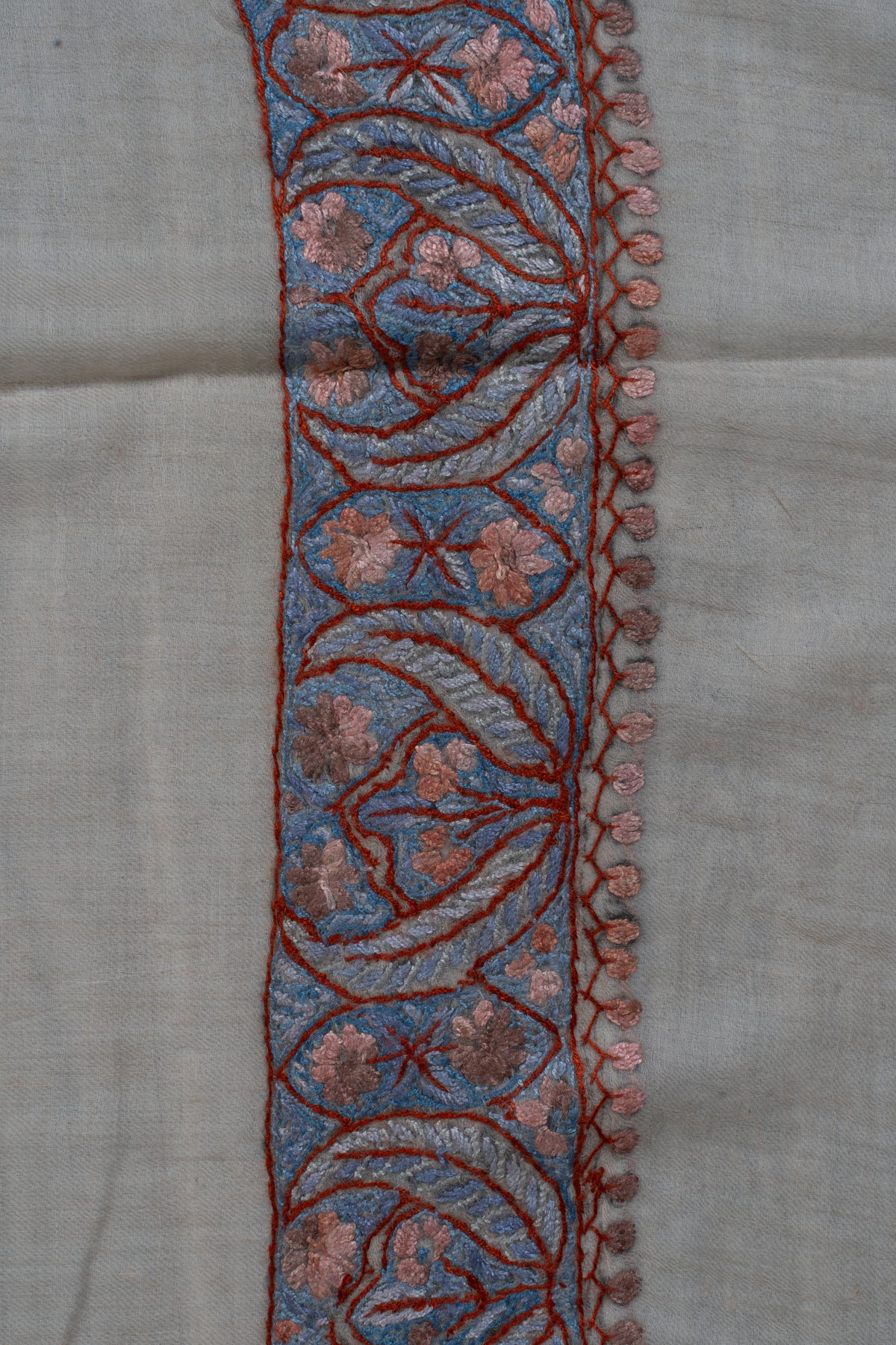 Close-up of a blue and dusky-rose Sozni border with curling leaves, small flowers and fine leaf edging on beige cashmere.