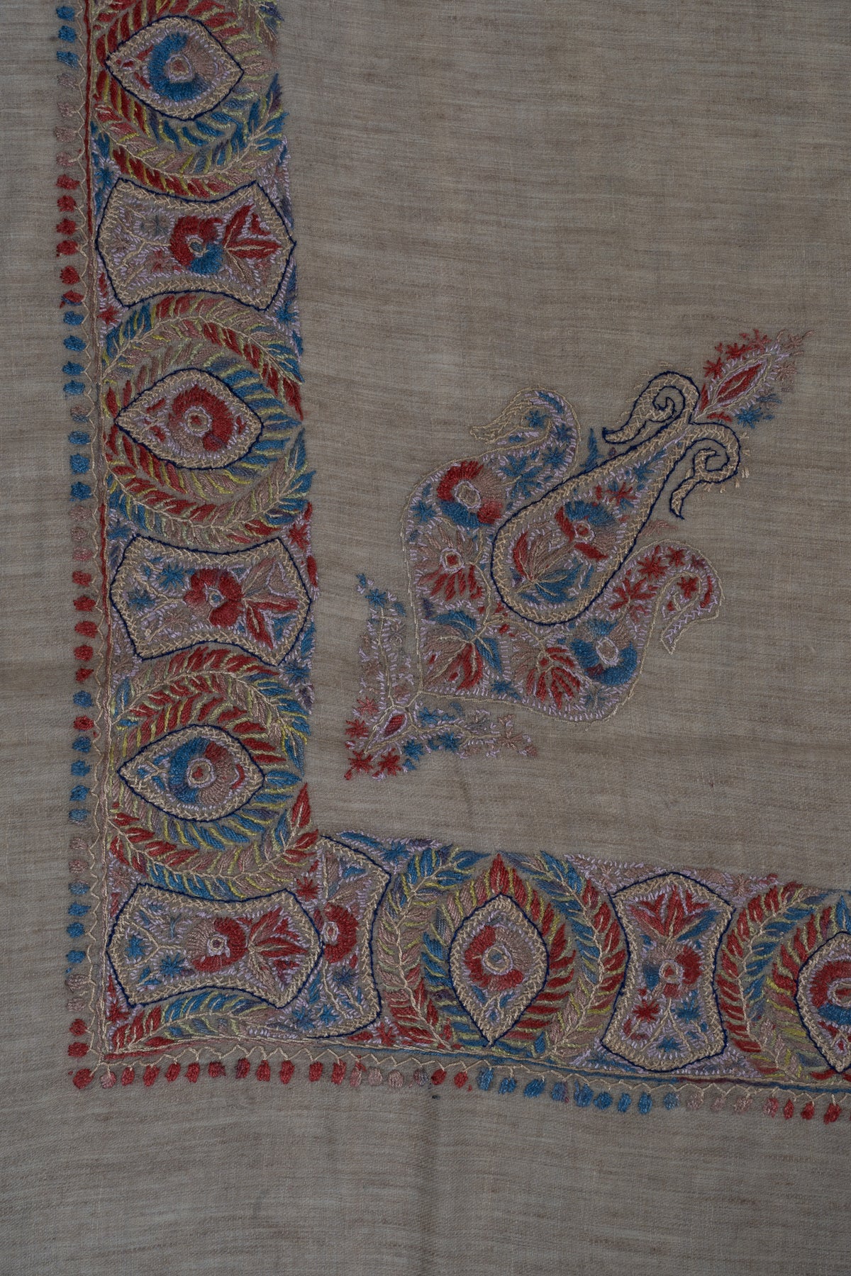Taupe rumal corner with a crimson-blue geometric border and a smaller curled floral motif