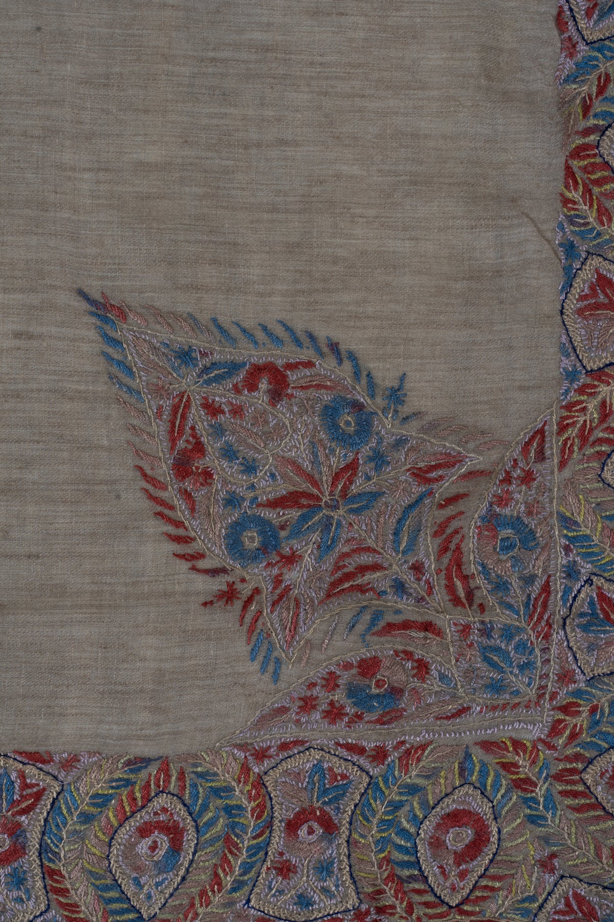 Close-up of crimson and blue flowers and fern-like leaves in the rumal's large corner design