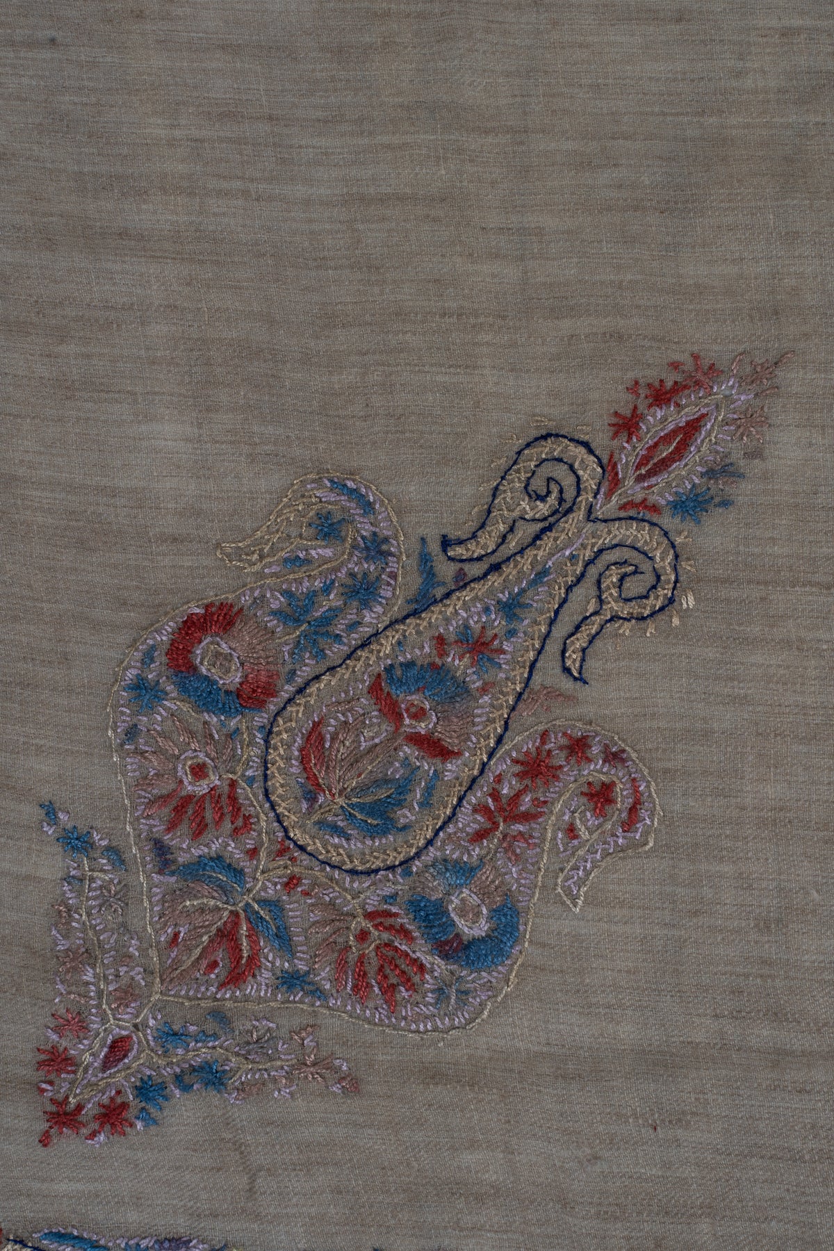 Close-up of the smaller curled floral motif with crimson and blue accents on taupe cashmere