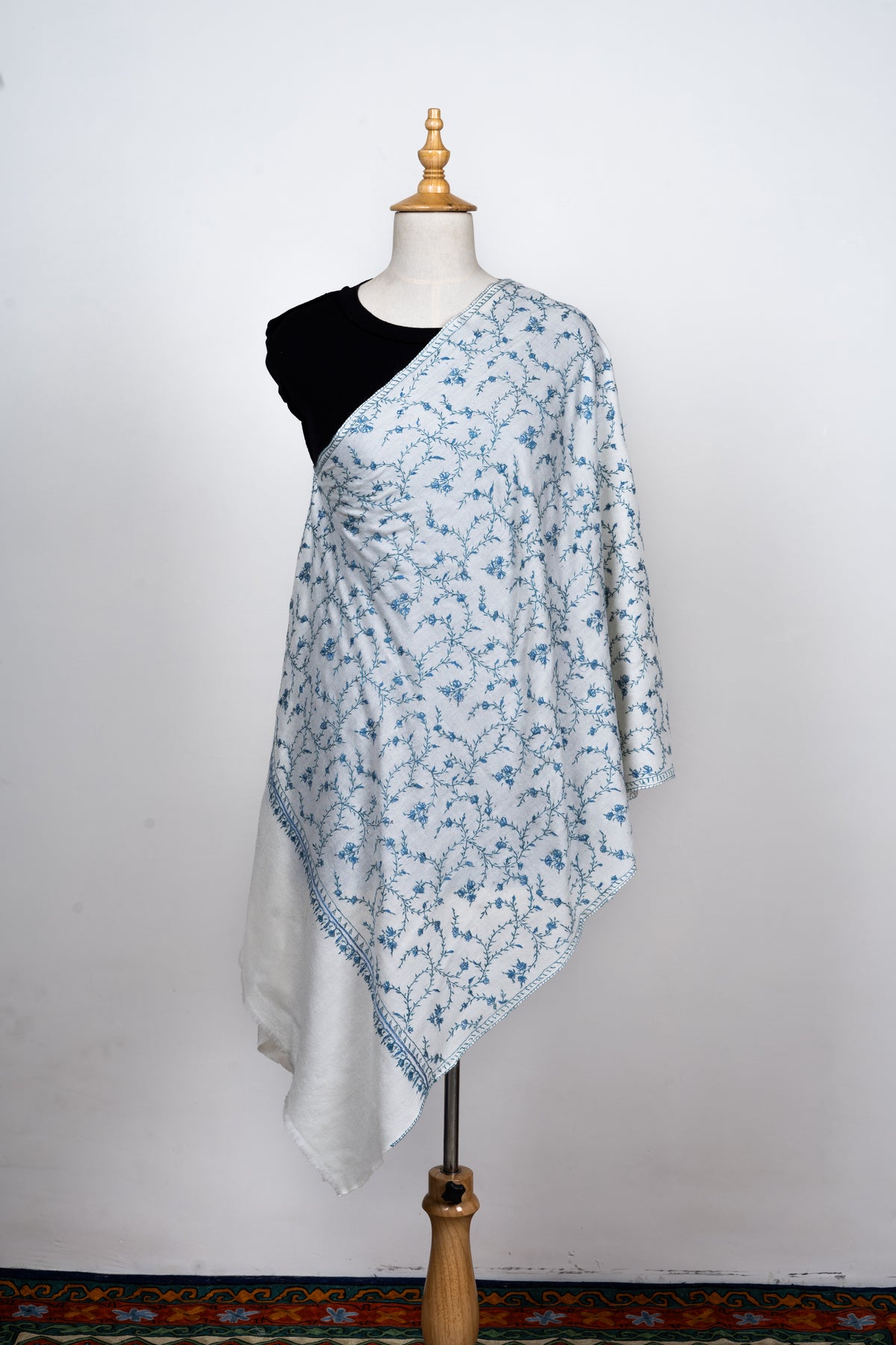 Front view of an ivory stole on a mannequin, covered in fine blue Sozni flowers and curling stems