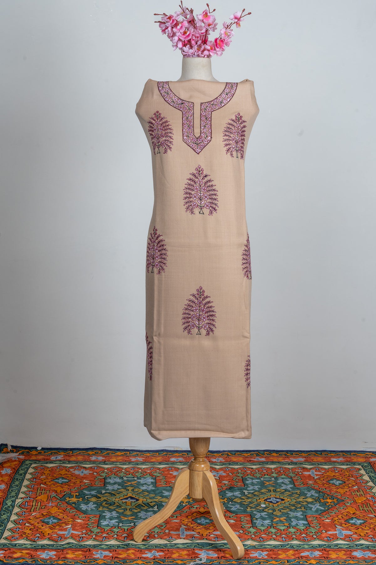 Full-length view of sand-beige suit fabric on a mannequin, showing a rose-pink embroidered neckline and scattered trees