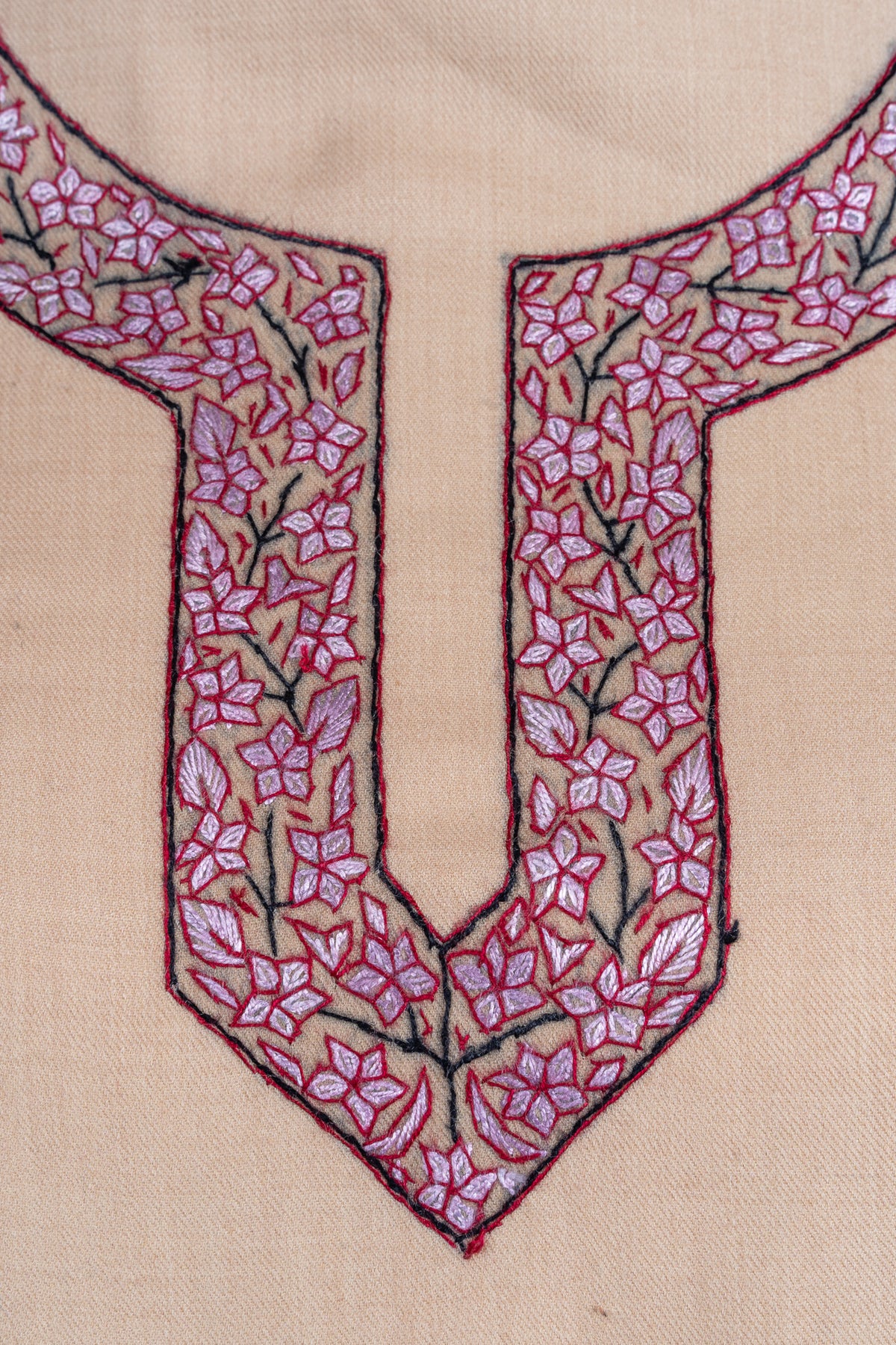 Close-up of rose-pink flowers and dark outlines around a rounded slit neckline on sand-beige suit fabric