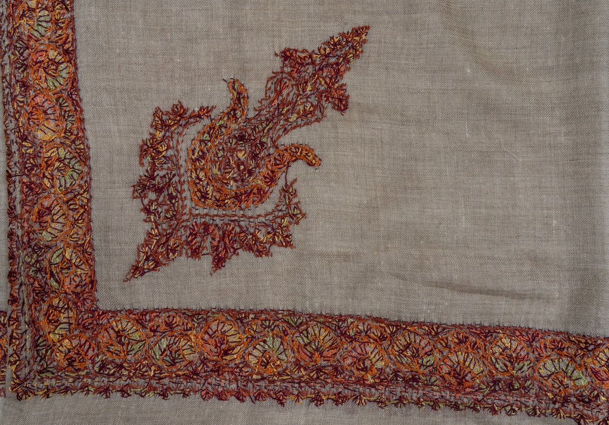 Close-up of a rumal corner showing fine red and orange stitching in the paisley and floral border