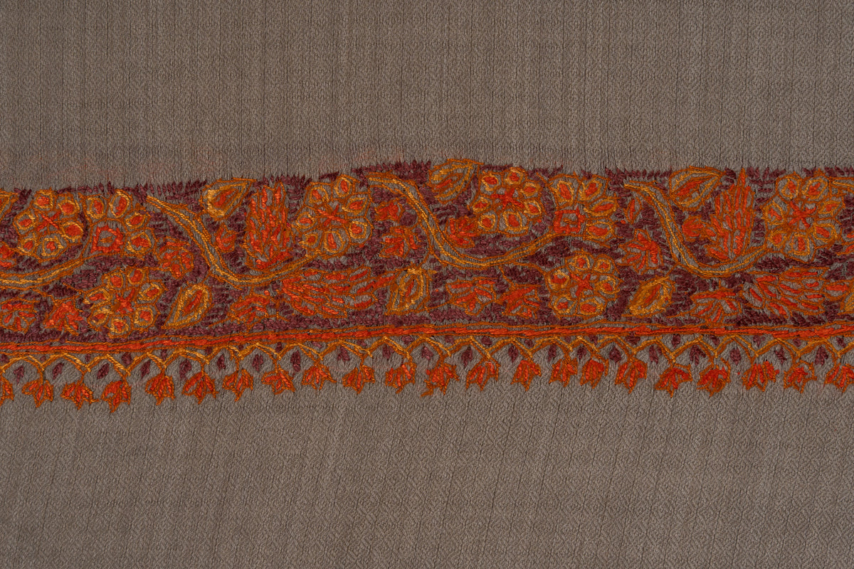 Close-up of orange-red Sozni flowers and curling vines above a row of pendant motifs on grey-beige fabric