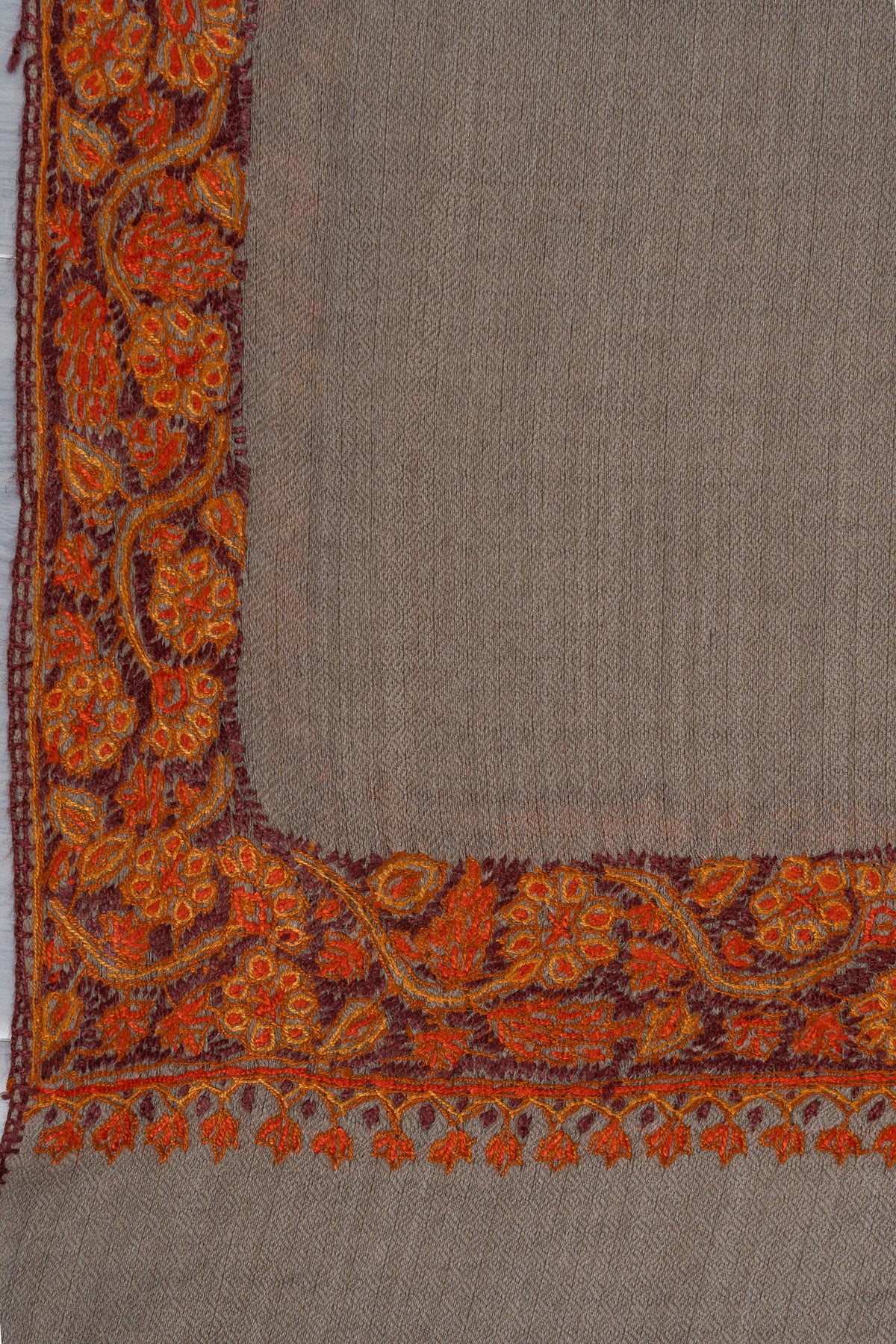 Grey-beige shawl corner laid flat with orange-red Sozni floral borders meeting around the plain woven field