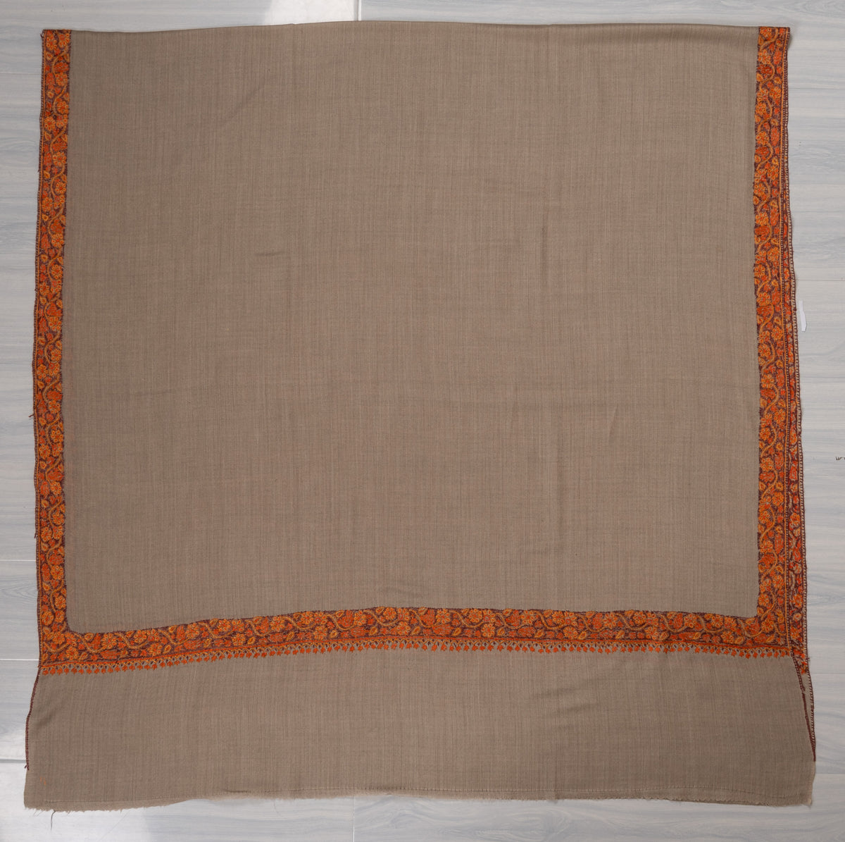 Grey-beige shawl laid flat with a plain centre, narrow orange-red Sozni borders and an unembroidered end margin