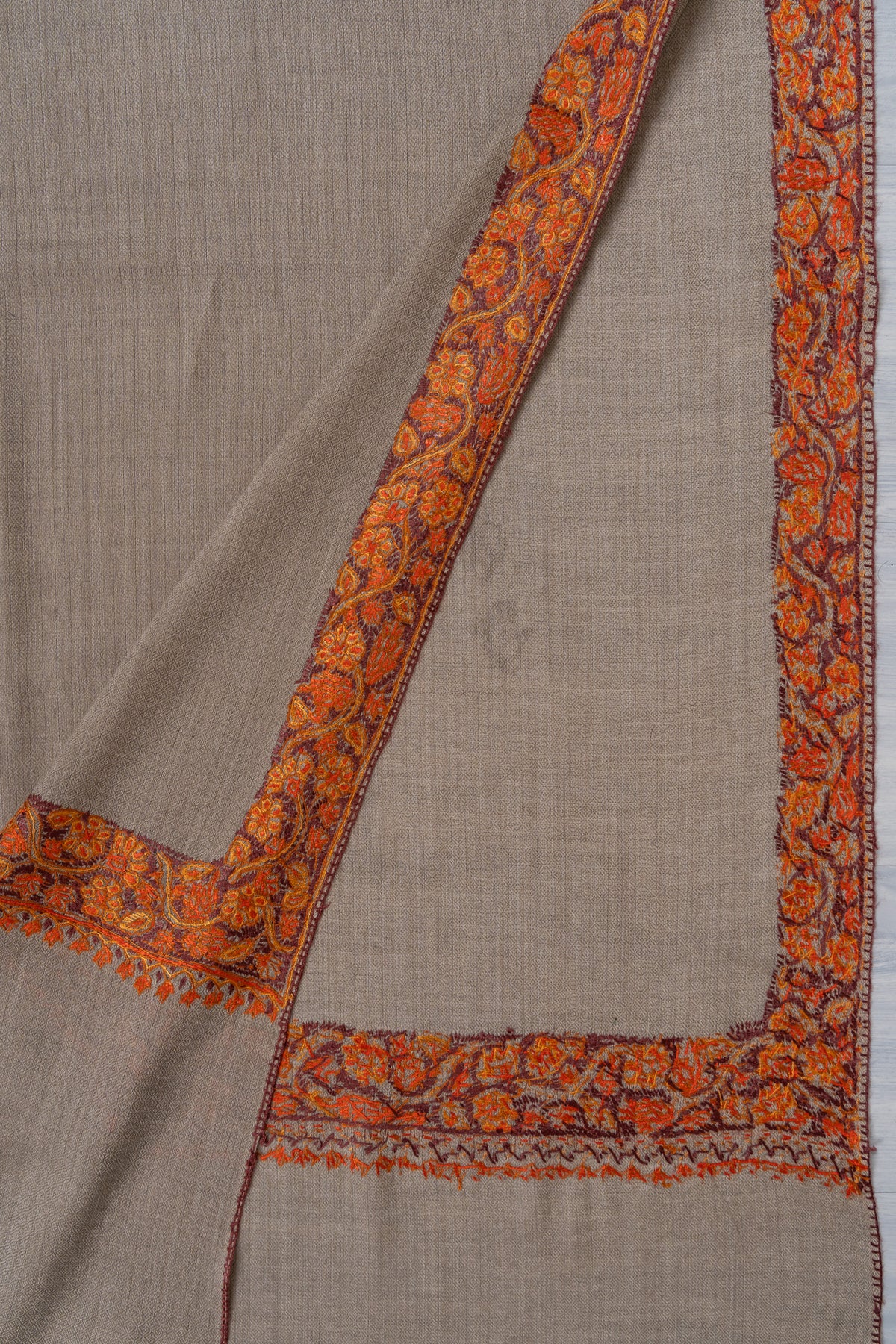 Folded grey-beige shawl corner revealing both sides of the orange-red Sozni floral border