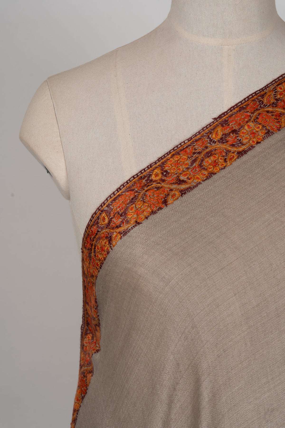 Shoulder detail of a grey-beige shawl with orange-red flowers and fine curling Sozni vines along the border
