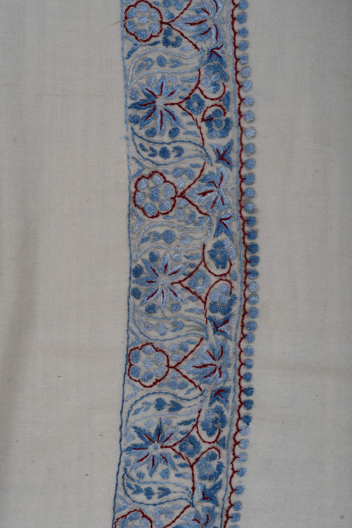 Close-up of powder-blue Sozni flowers and curling vines with burgundy outlines along an ivory Merino wool rumal border.