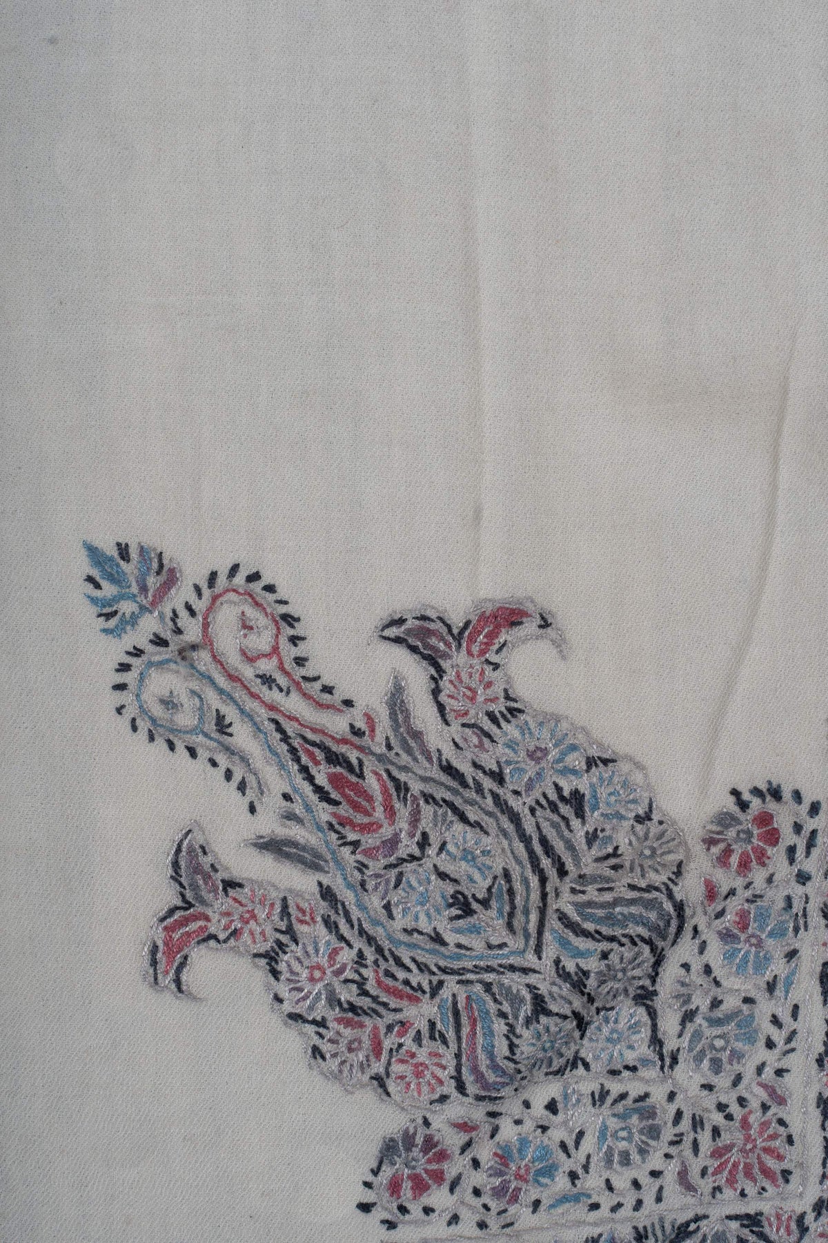 Close-up of the large curled floral motif with rose and blue accents on ivory wool